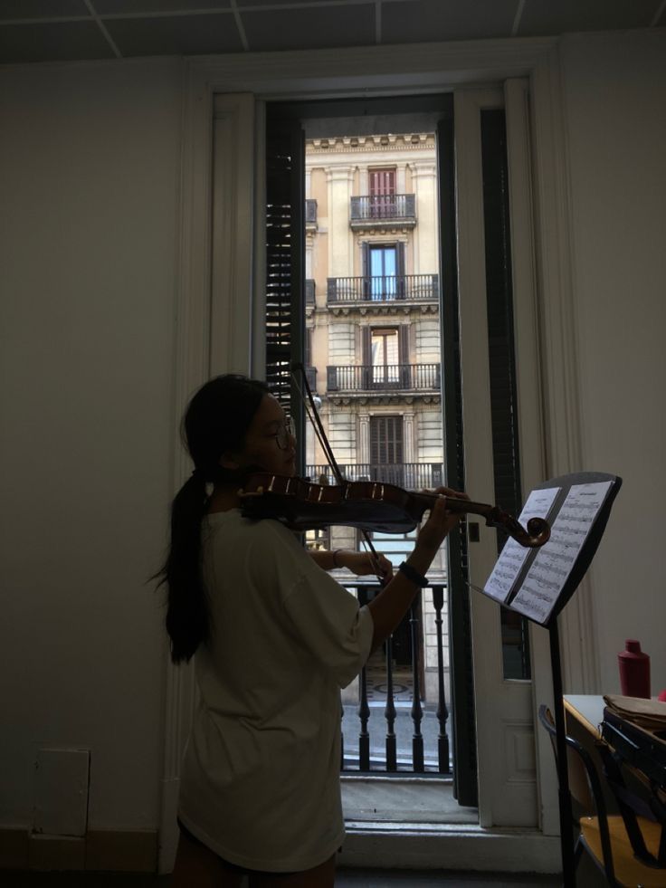 a woman playing the violin in front of a window