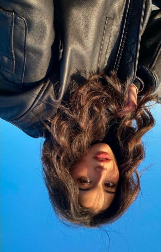 a woman is upside down in the air with her hair hanging over her head and wearing black leather jacket