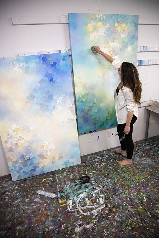 a woman standing in front of two paintings on easels with paint chips all over the floor