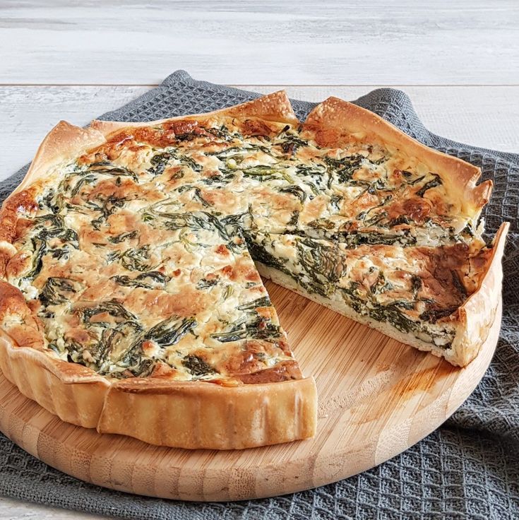 a cheese and spinach quiche on a wooden platter with a slice missing