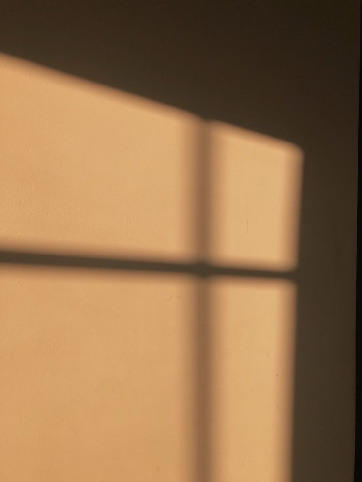 an orange clock sitting on top of a wooden table next to a wall with a shadow cast on it