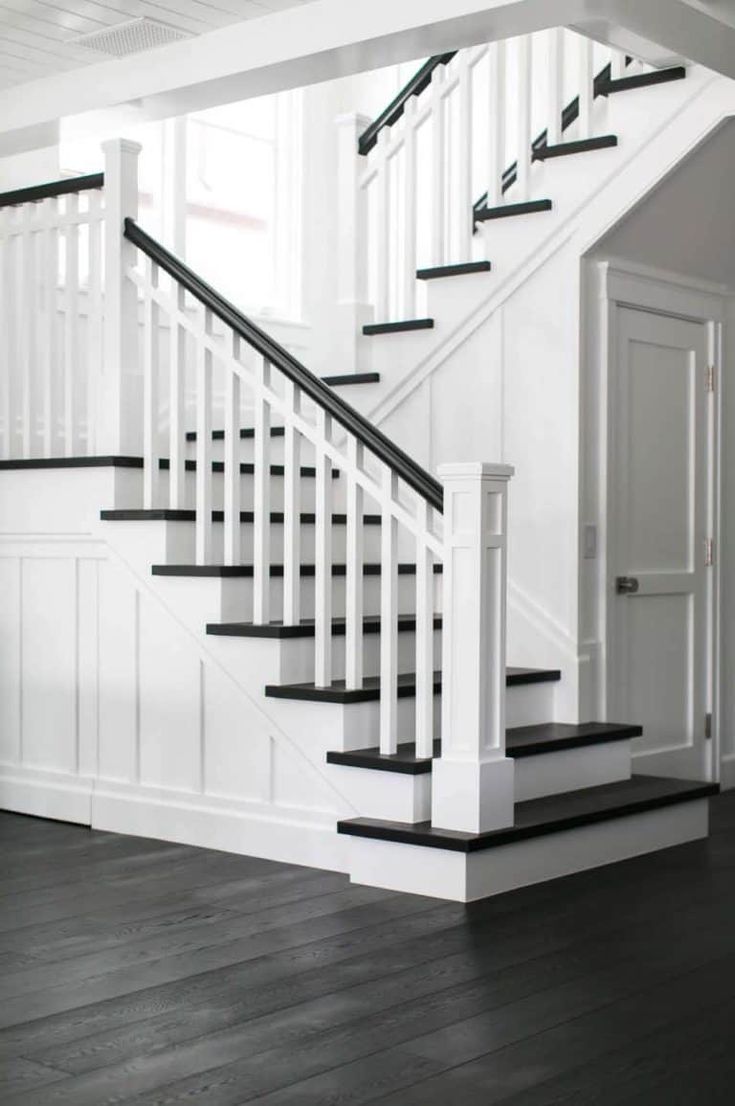 a white staircase with black railing and wood flooring