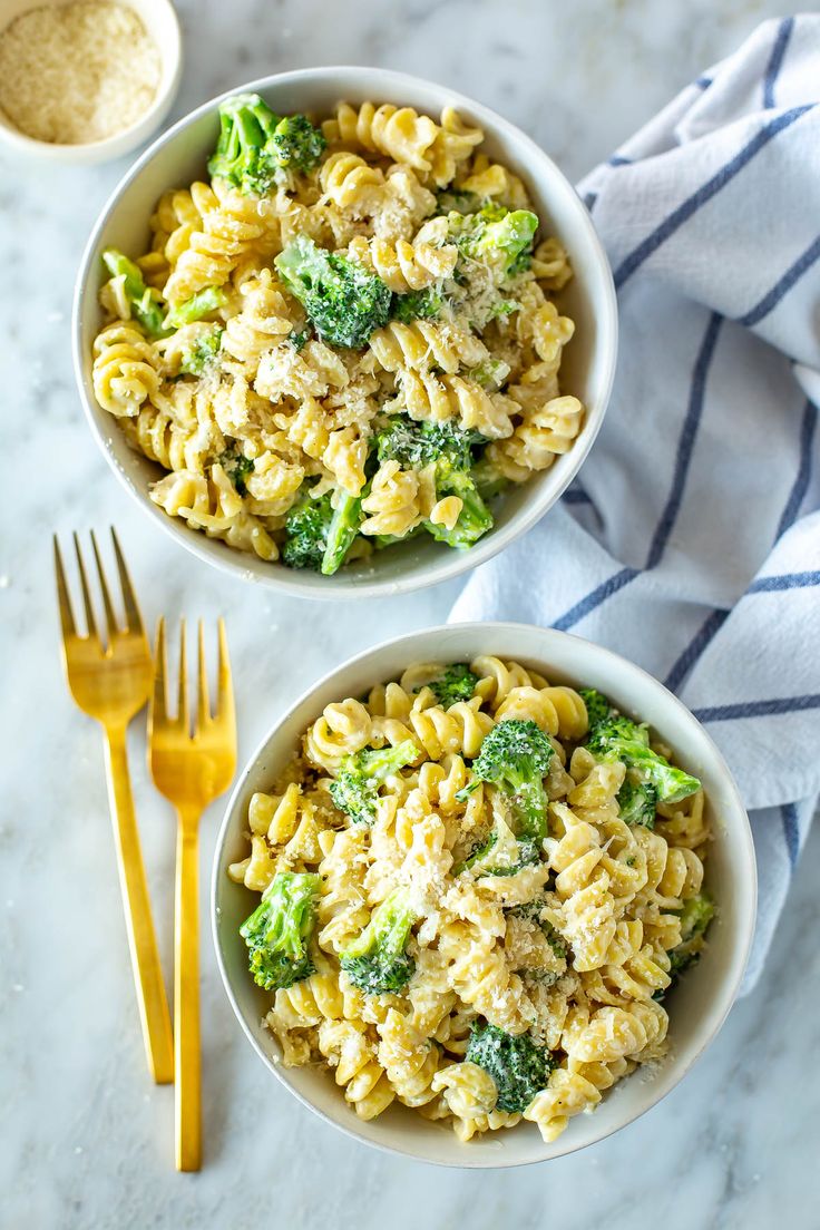 two bowls filled with pasta and broccoli on top of a marble countertop