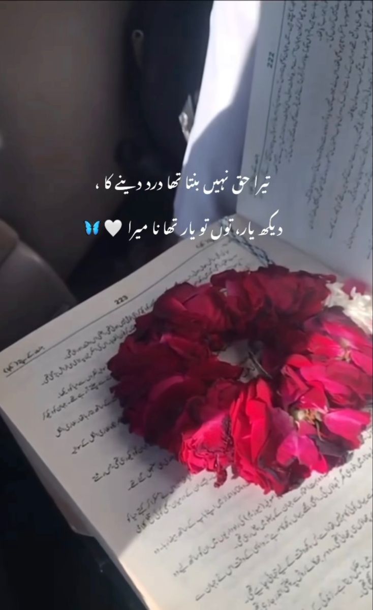 an open book with writing on it and red flowers in the middle, sitting on a table