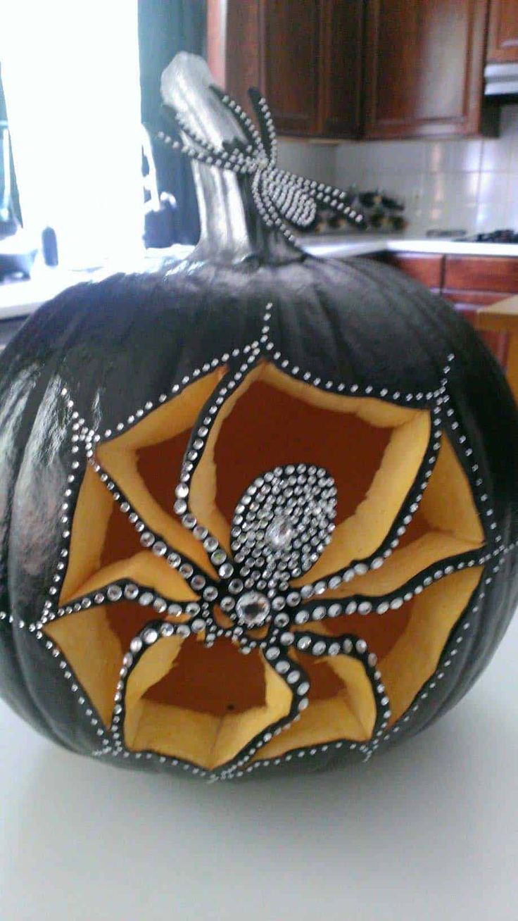 a black pumpkin decorated with an intricate spider web and diamond accents on the top, sitting on a kitchen counter