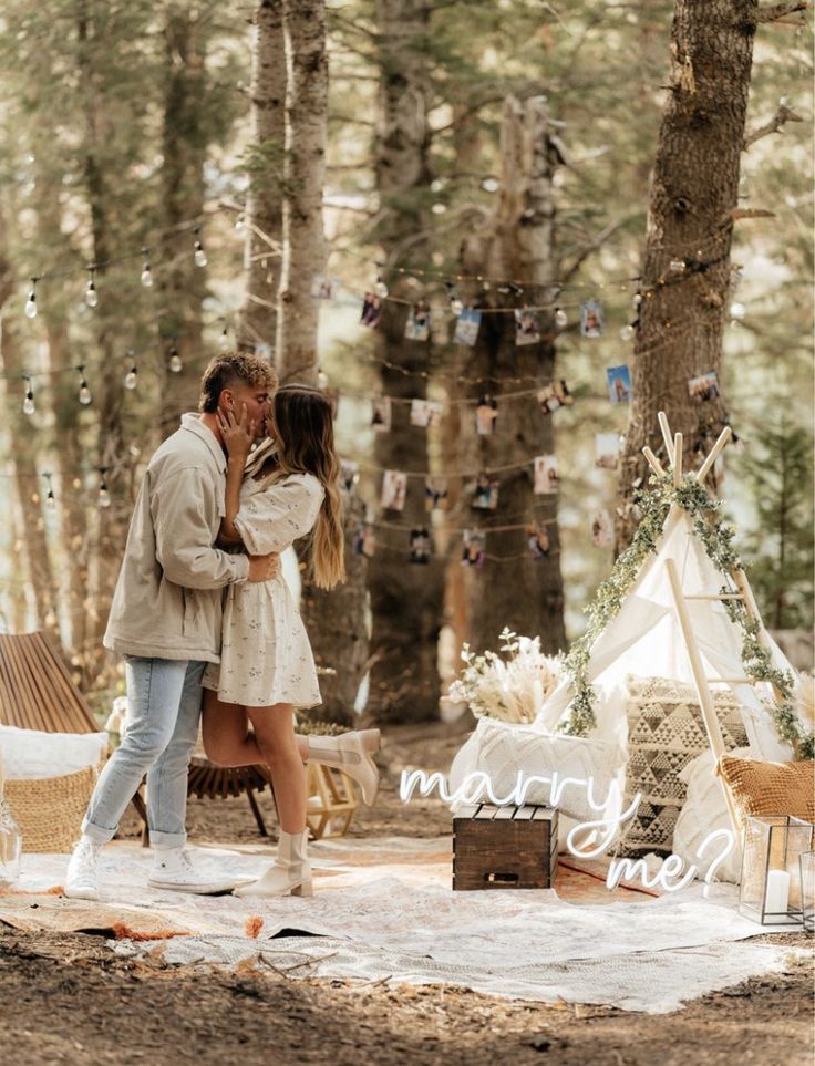 a man and woman standing in the woods near a teepee with lights strung from it