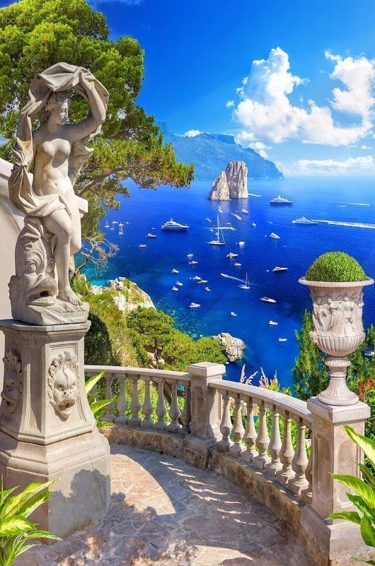 a statue on top of a balcony next to the ocean with boats in the water