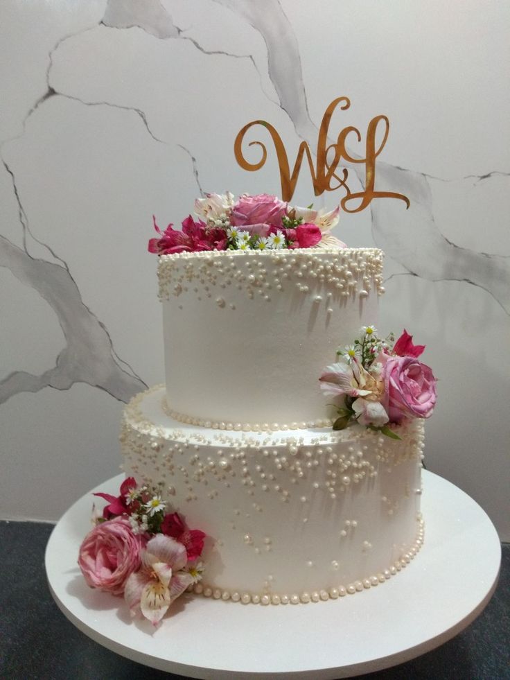 a three tiered wedding cake with pink flowers and monogrammed initials on top