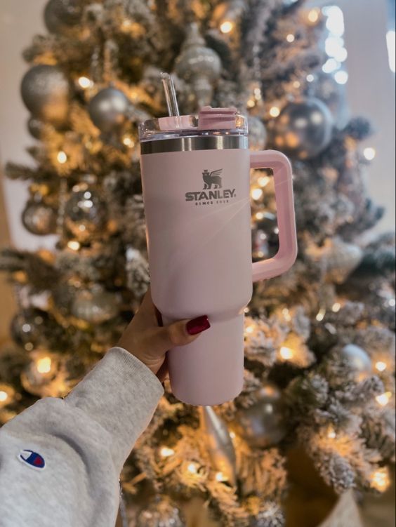 a person holding a pink coffee cup in front of a christmas tree