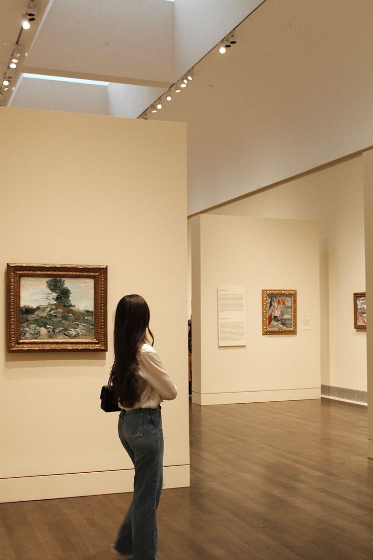 a woman standing in an art gallery looking at paintings