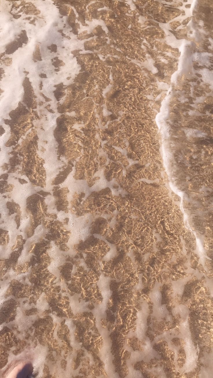 someone is standing in the water at the beach with their feet up on the sand