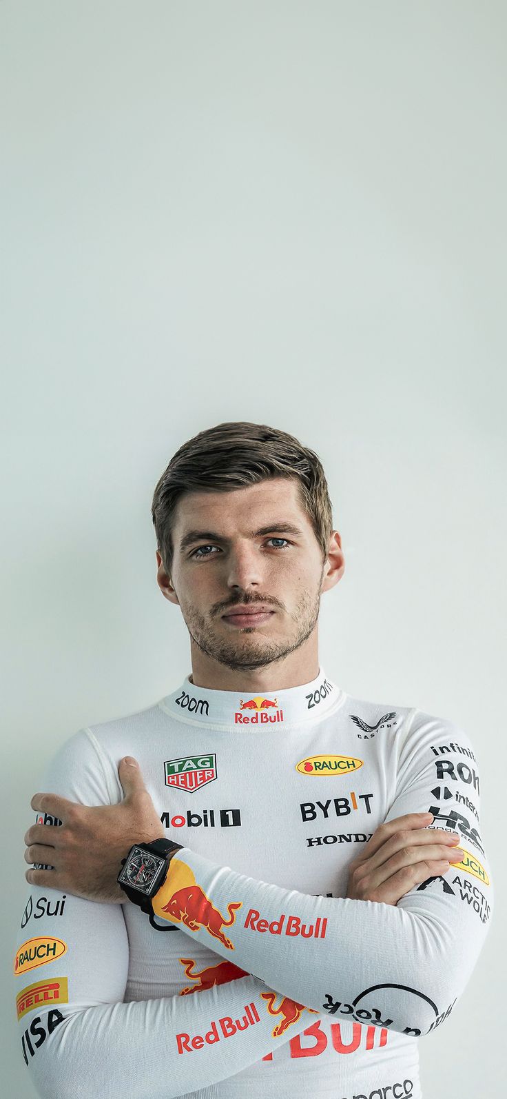 a man with his arms crossed standing in front of a white wall wearing a red bull jersey