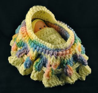 a crocheted baby doll in a blanket on a black background with a wooden toy