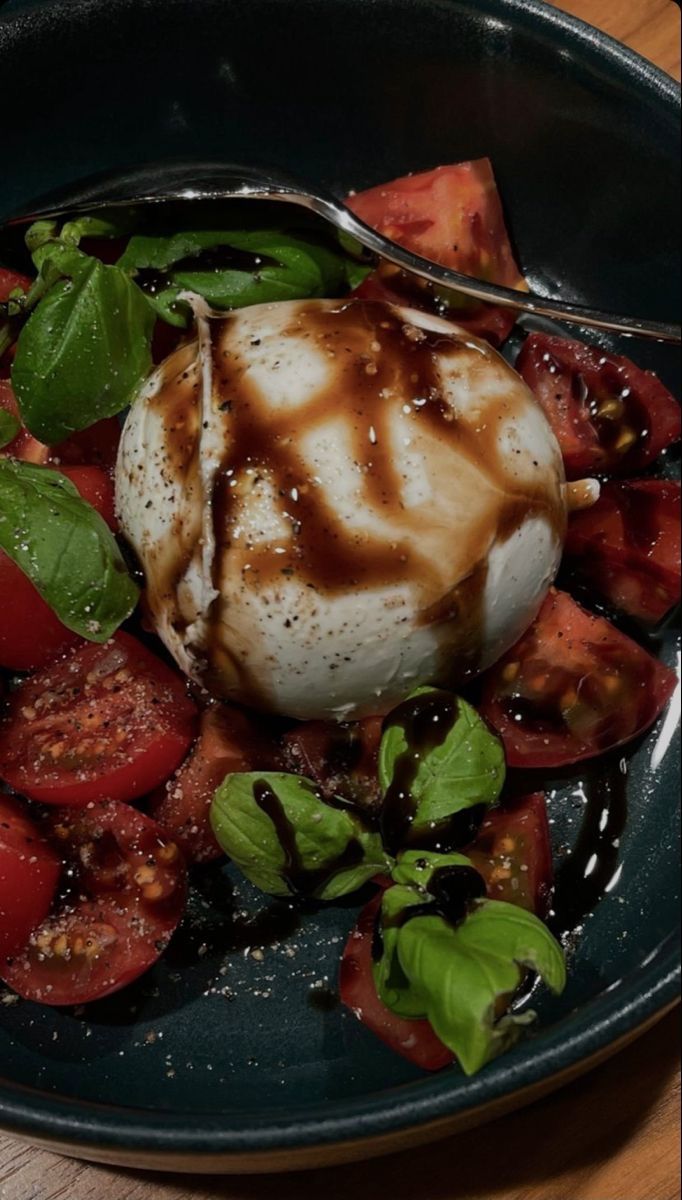 a black plate topped with lots of food on top of a wooden table next to a fork