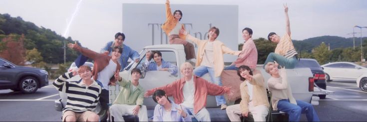 a group of people sitting on the back of a truck in a parking lot with their arms up