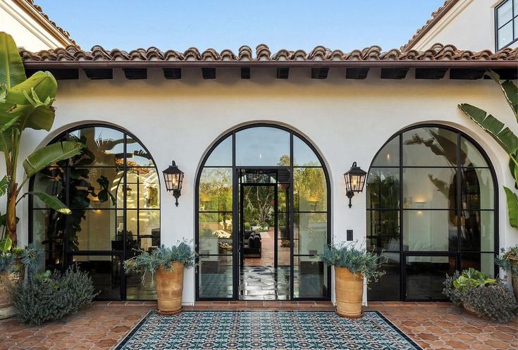 an entrance to a home with potted plants and large windows on the side of it