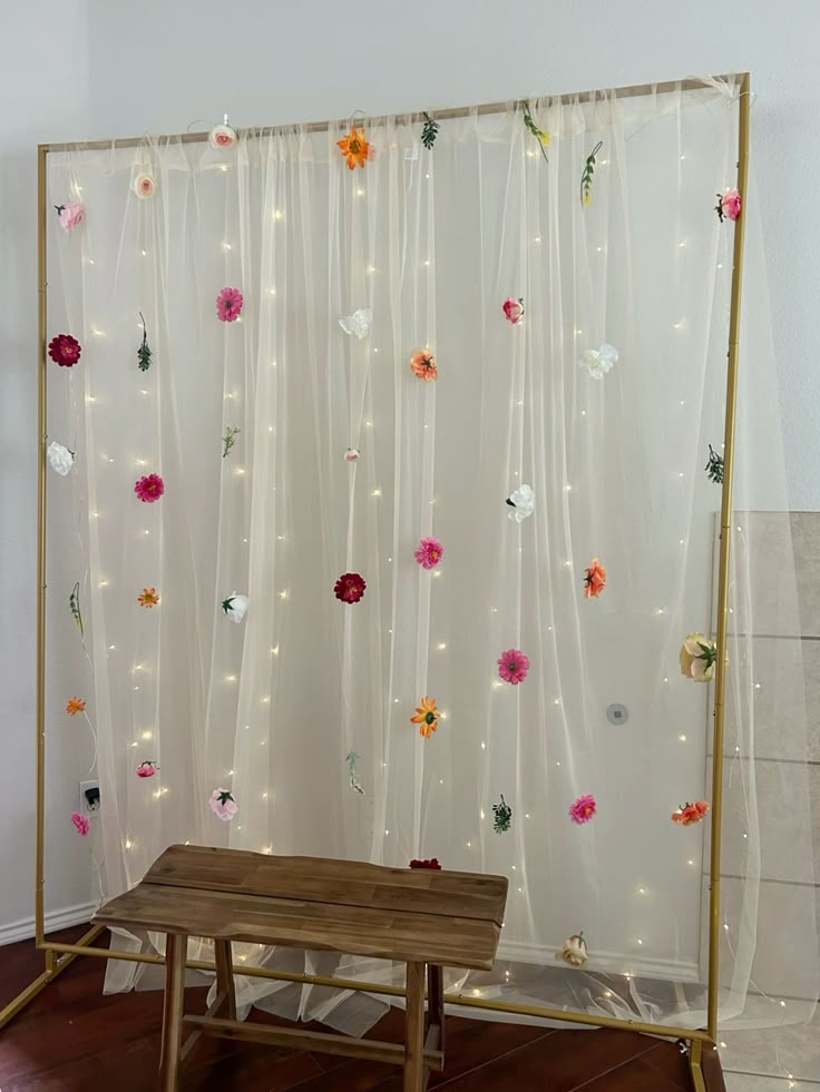 a wooden table sitting in front of a white curtain with flowers on it's side