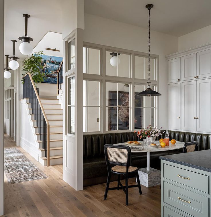 a kitchen and dining room with white cabinets, wood floors and black leather bench in the center