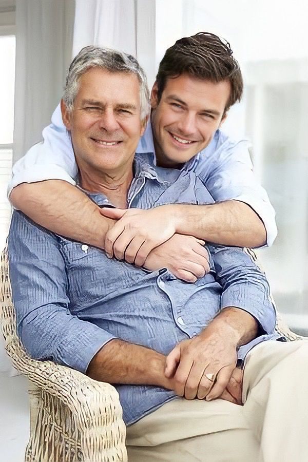 two men hugging each other while sitting on a chair