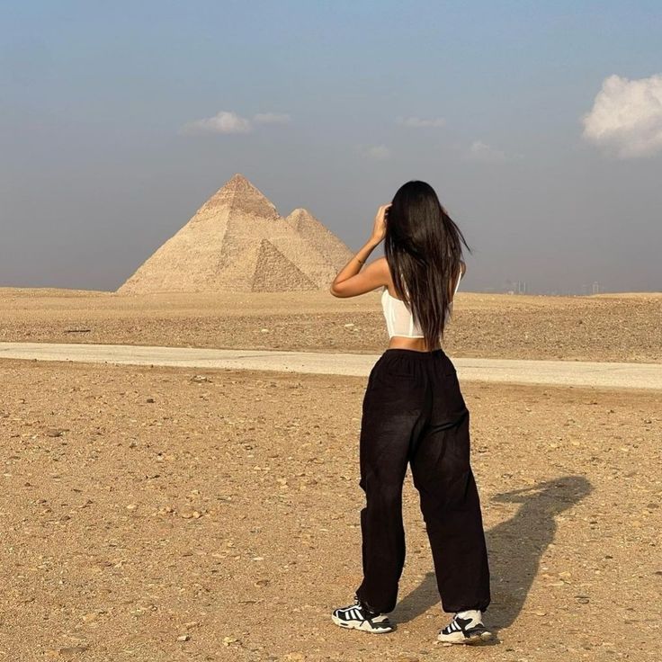 a woman standing in the desert looking at pyramids