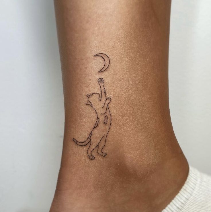 a small tattoo on the ankle of a woman with a cat reaching up at the moon