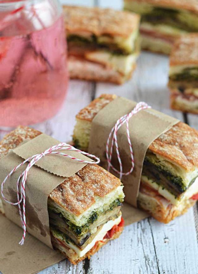 sandwiches wrapped in brown paper sitting on top of a wooden table next to a mason jar