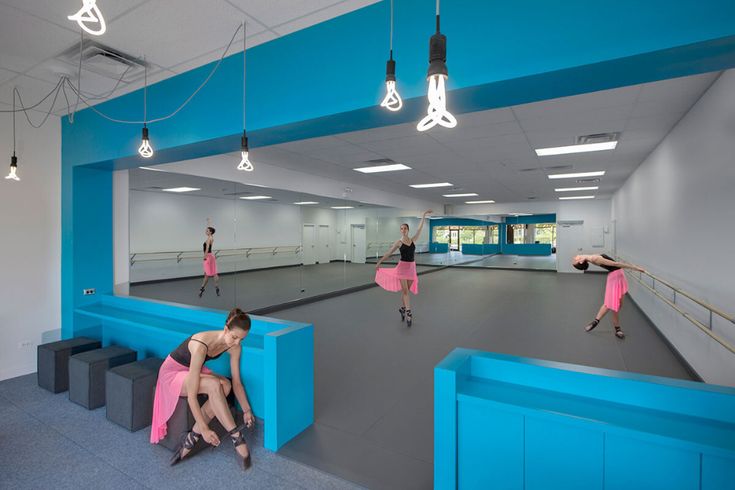 people are sitting on benches in an empty room with blue walls and lights hanging from the ceiling