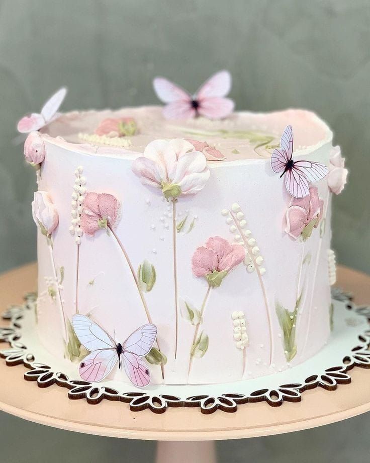 a white cake with pink flowers and butterflies on it sitting on a table next to a wall