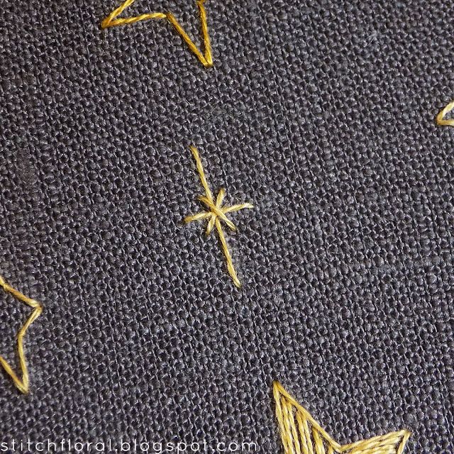 some yellow stars are on a black fabric with white stitching and gold thread in the middle