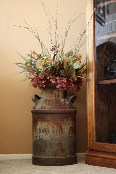 a rusted vase with flowers in it sitting on the floor next to a mirror