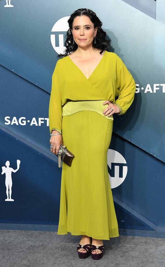 a woman in a long green dress standing on a gray carpet with her hands on her hips