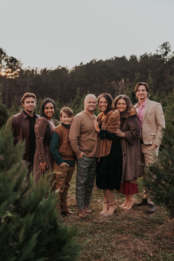 a group of people standing next to each other in front of a tree line at sunset