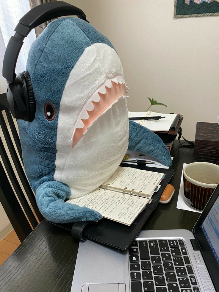 a stuffed shark with headphones sitting in front of a laptop