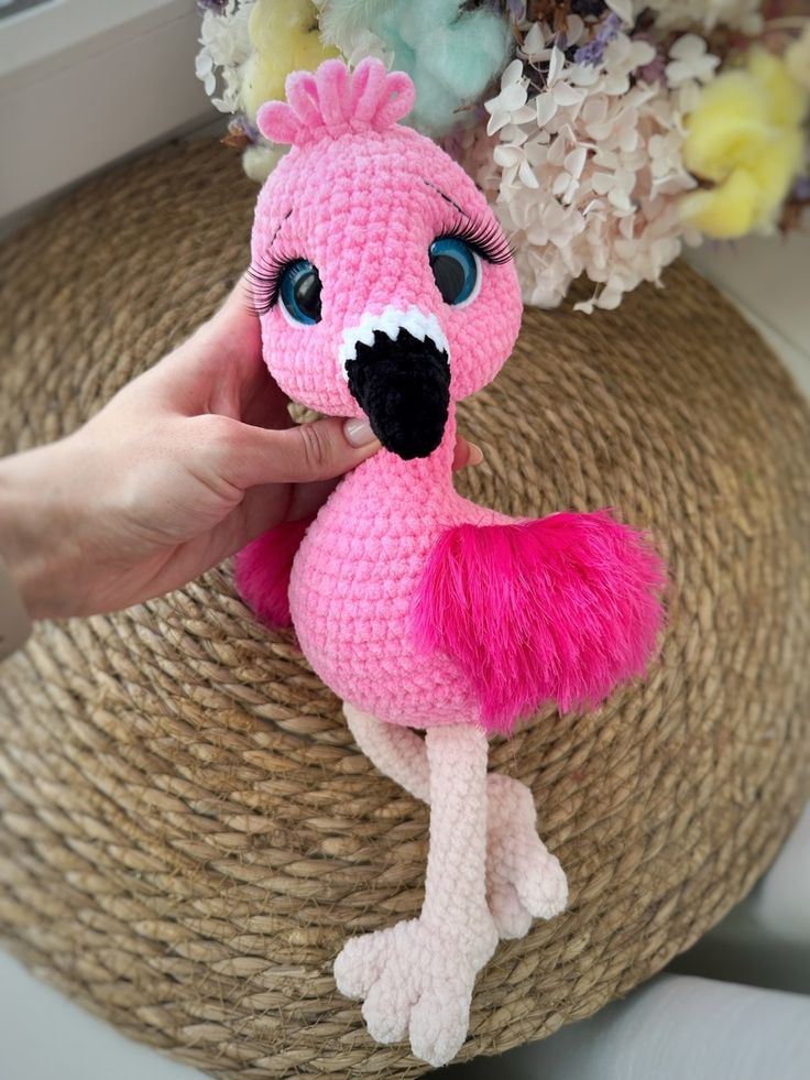 a pink crocheted flamingo stuffed animal sitting on top of a wicker basket