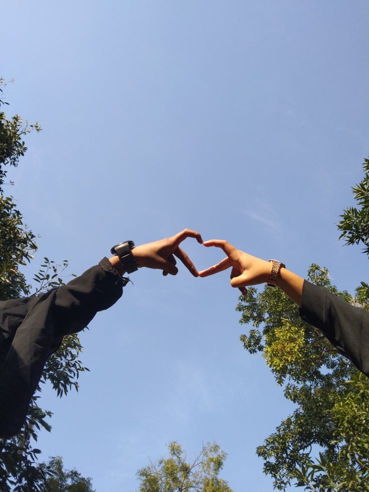 two hands making a heart shape with their fingers in front of some trees and blue sky