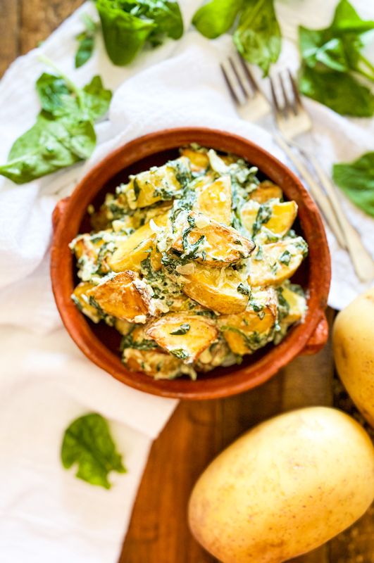 a wooden bowl filled with food next to two pears and spinach on top of a table