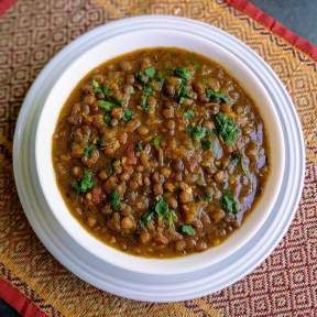 a white bowl filled with beans on top of a red and yellow place mat next to a spoon