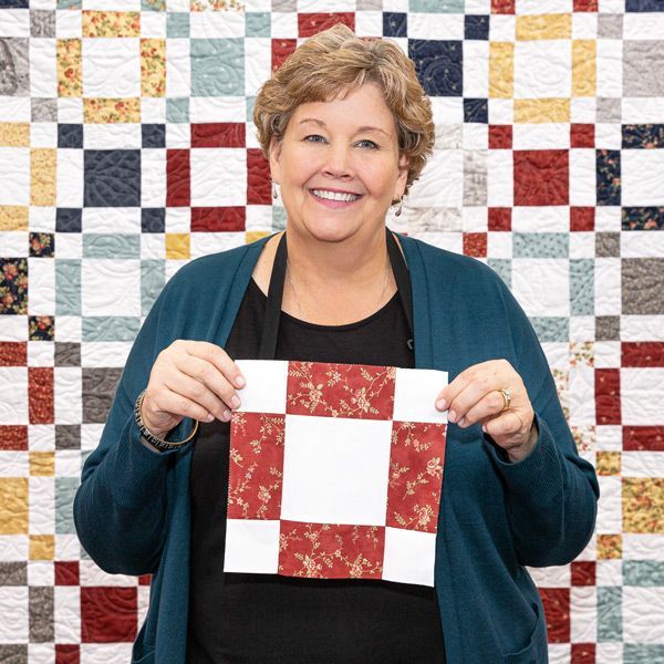 a woman holding up a piece of paper in front of a quilt