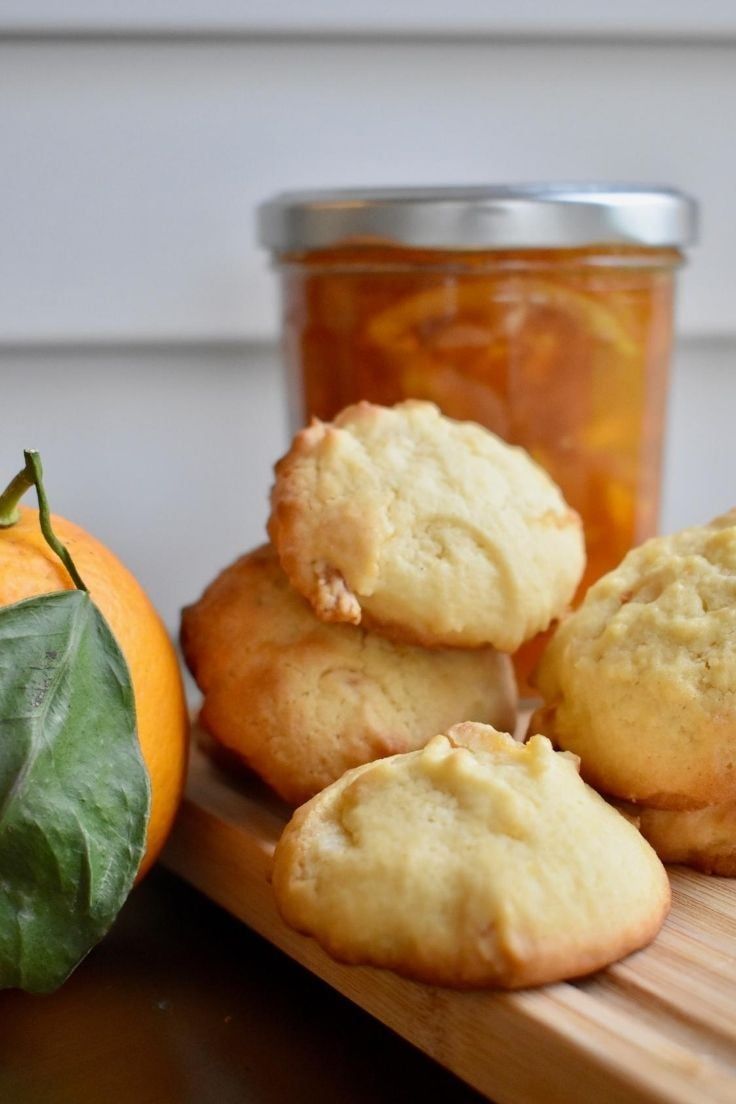 some muffins are on a cutting board next to an orange and a jar of jam