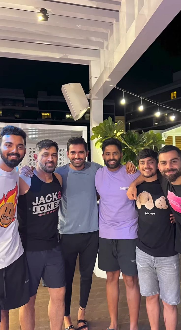 four men posing for a photo together in front of a building with lights and plants