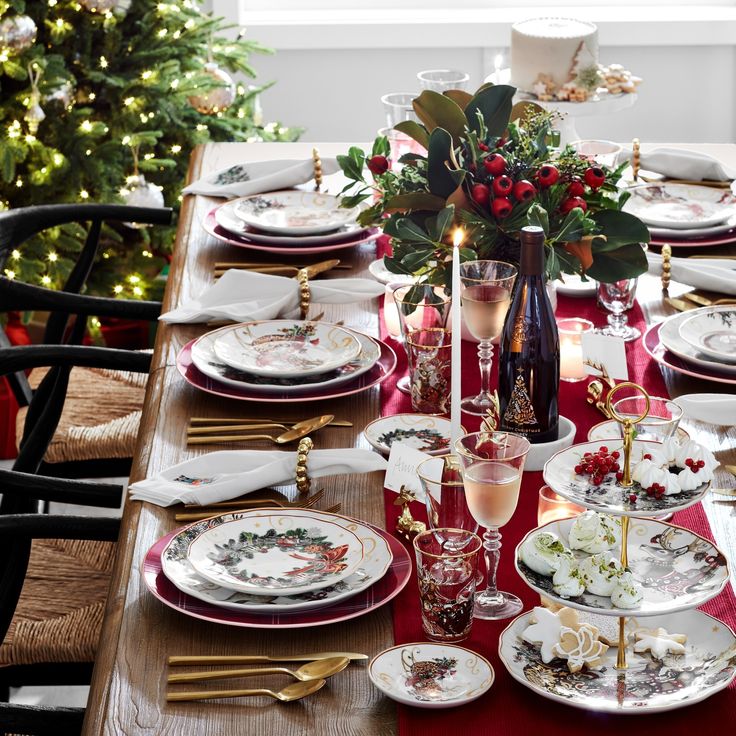 a table set for christmas dinner with plates, silverware and candlesticks on it