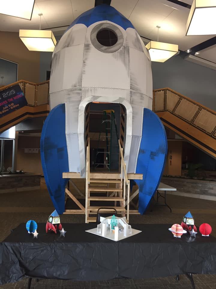 an inflatable space shuttle is on display at a convention or event with tables and chairs around it