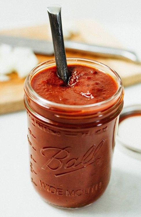 a glass jar filled with red liquid sitting on top of a white table next to spoons