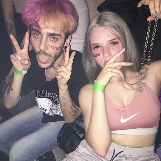 two people with pink hair and piercings posing for the camera, one is making peace signs