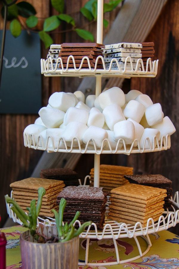 a three tiered cake stand with cookies and marshmallows on it, next to a potted succulent plant