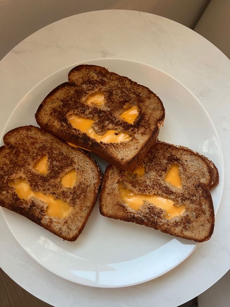 three pieces of toast with cheese on them sitting on a white plate next to a knife and fork