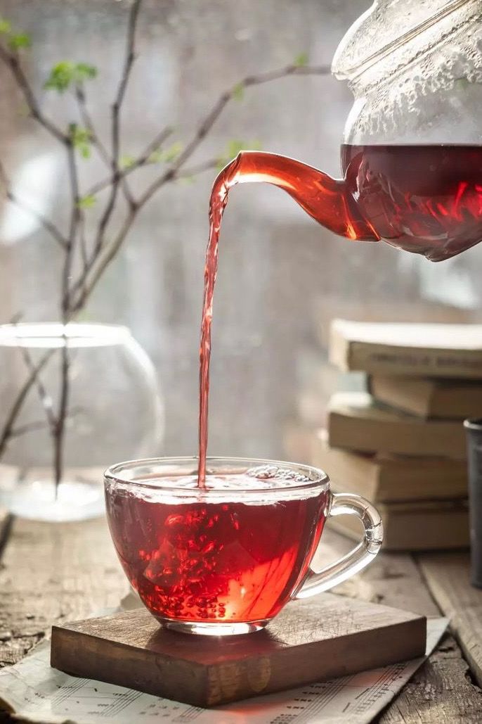 tea being poured into a glass cup on top of a wooden table next to books