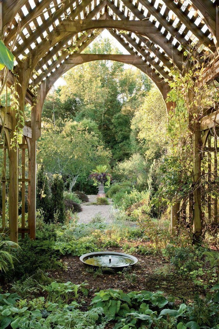 an arch in the middle of a garden with lots of trees and plants around it