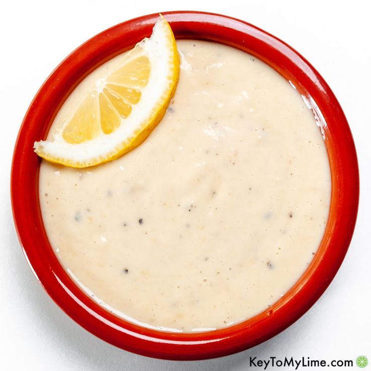 a red bowl filled with cream sauce and a slice of lemon