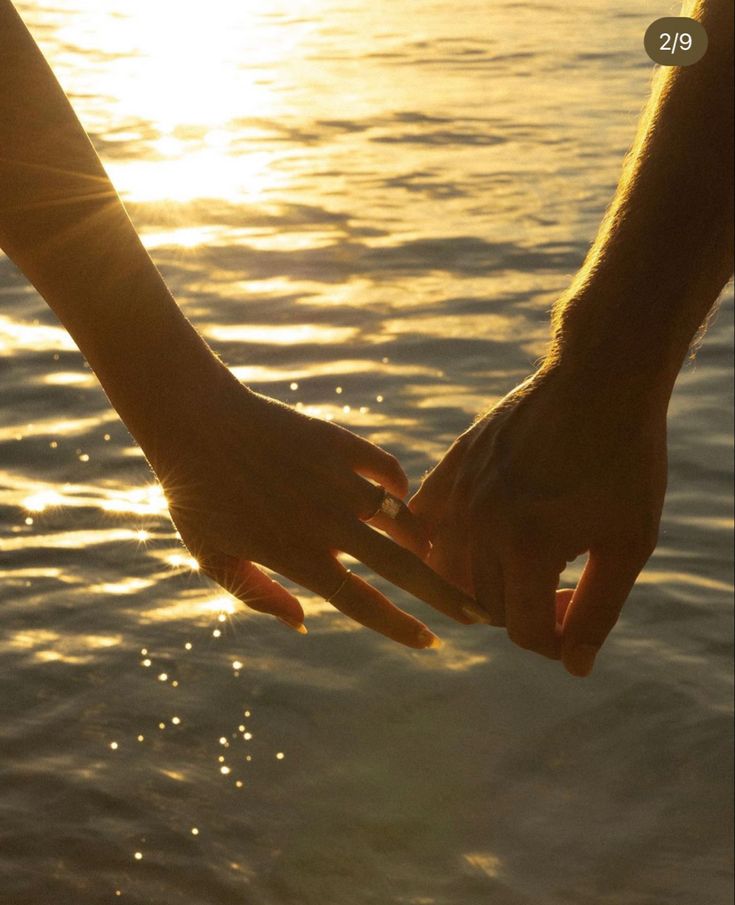 two people holding hands over water at sunset